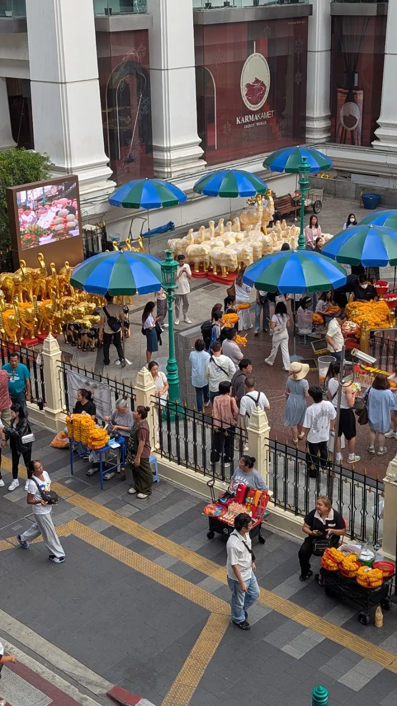 Gilded elephant votive figures, blue umbrellas, and marigold-garland vendors at the Erawan Shrine, Ratchaprasong