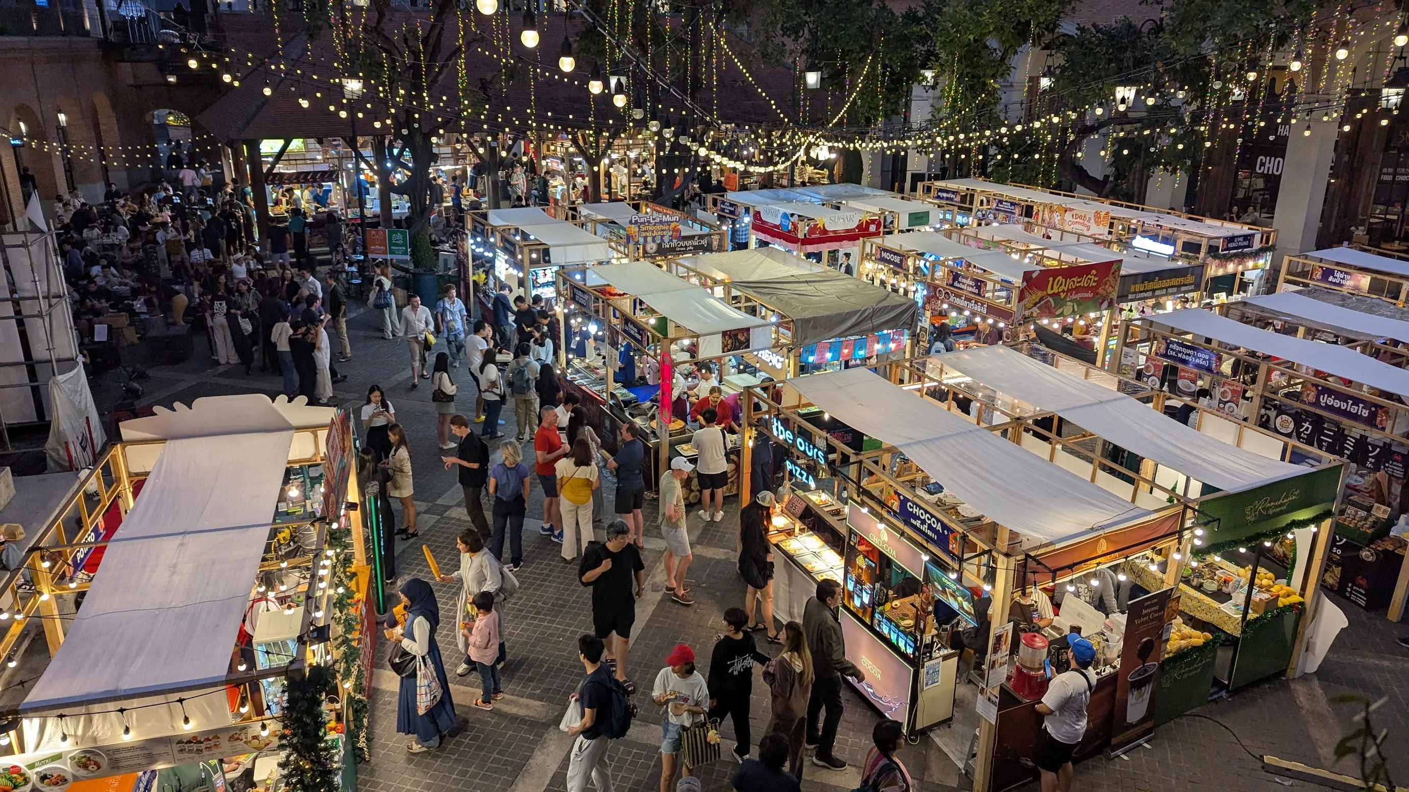 A night market from above: rows of lit food stalls under strings of bulbs