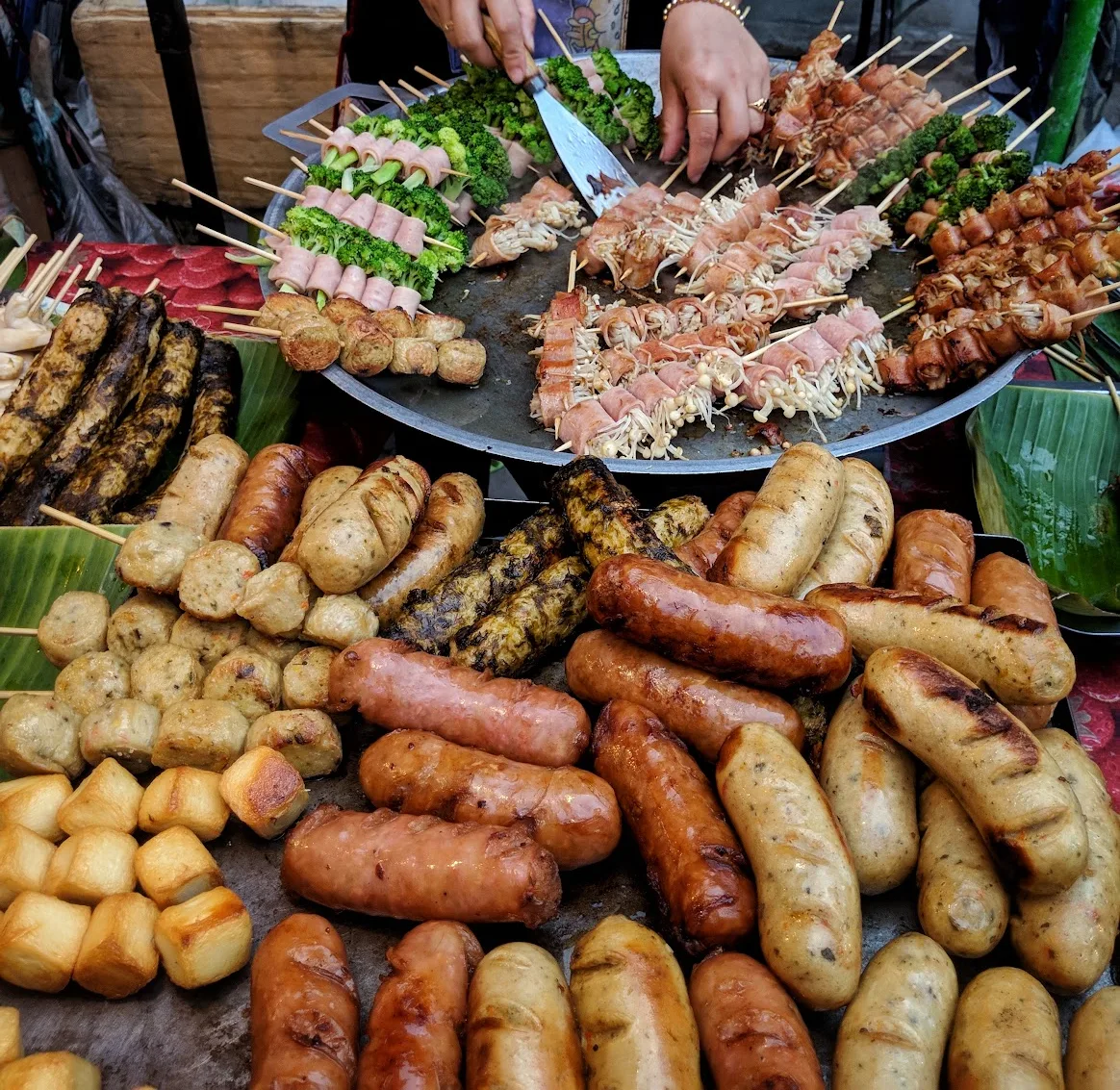 A street vendor turning skewers of pork, mushrooms and northern sausage on a charcoal grill