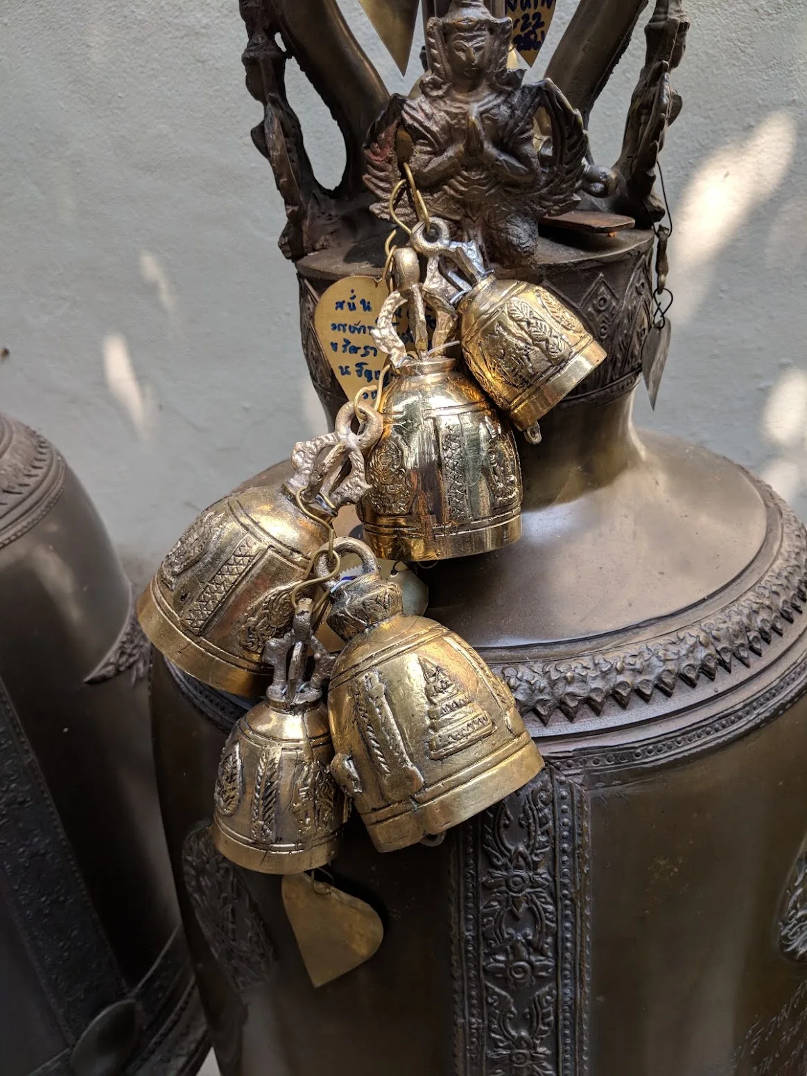 Brass temple bells strung from a bronze shrine figure with a handwritten Thai tag