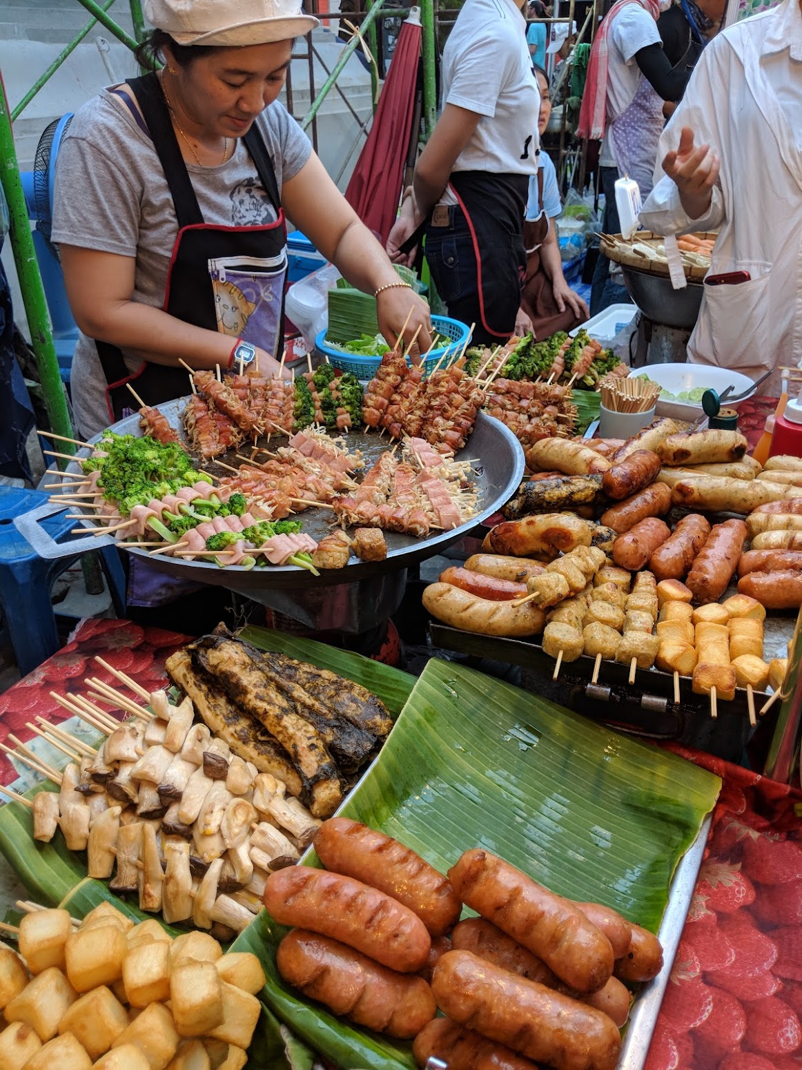 A Bangkok street-food stall with skewers, sausages, and grilled mushrooms