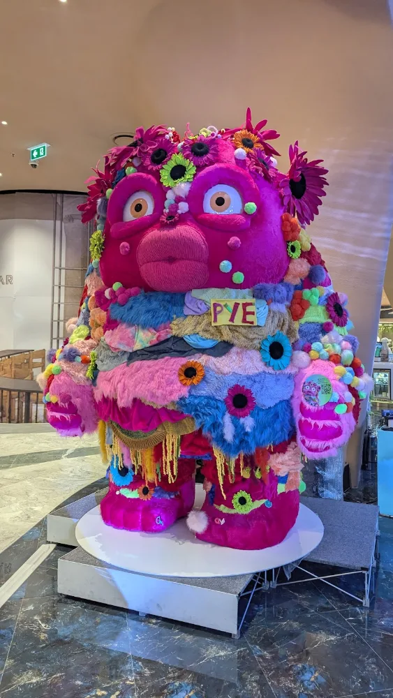 A giant pink furry PYE art-toy sculpture on display in a Bangkok mall