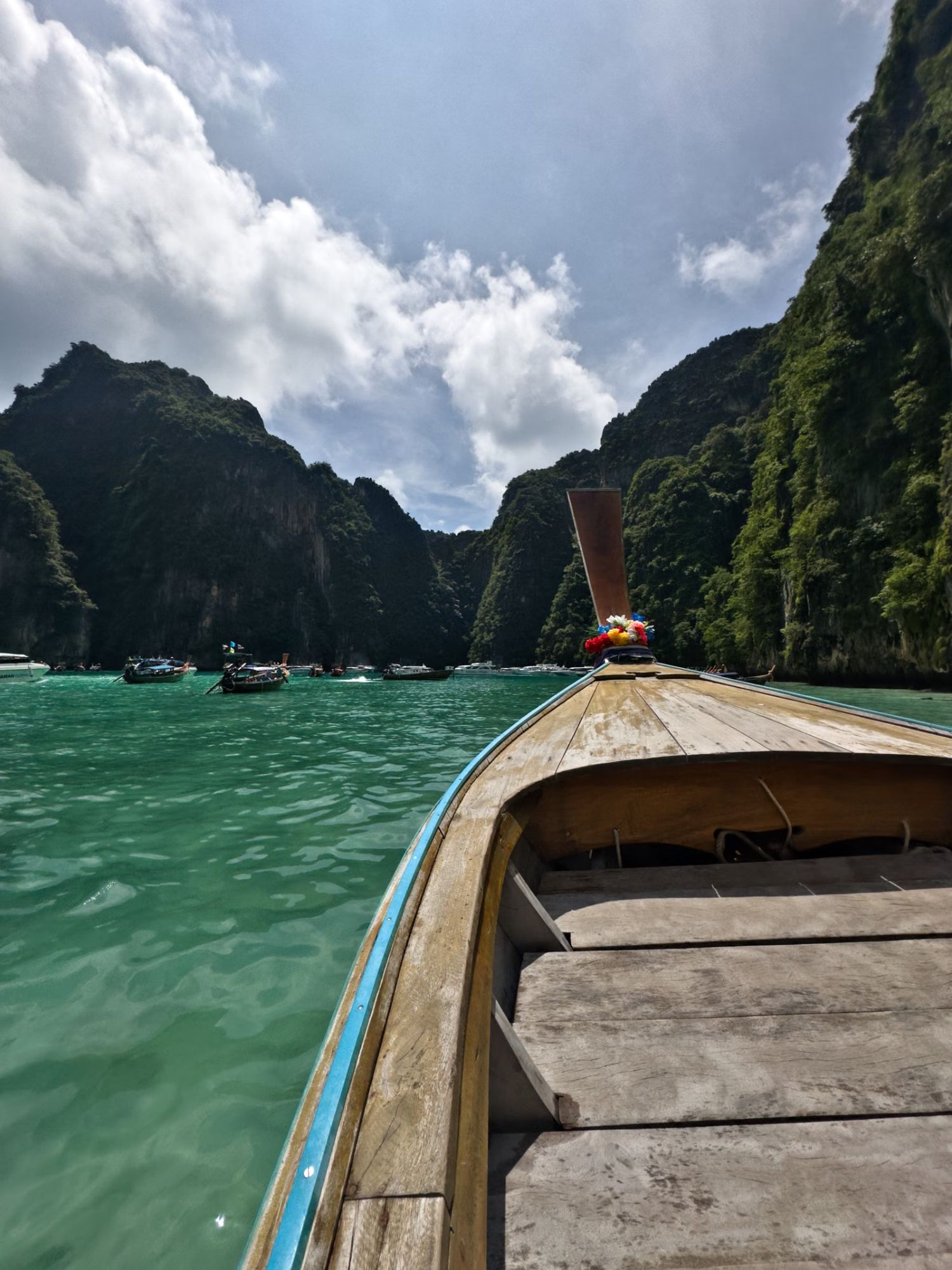 The bow of a longtail boat heading out toward limestone cliffs in southern Thailand