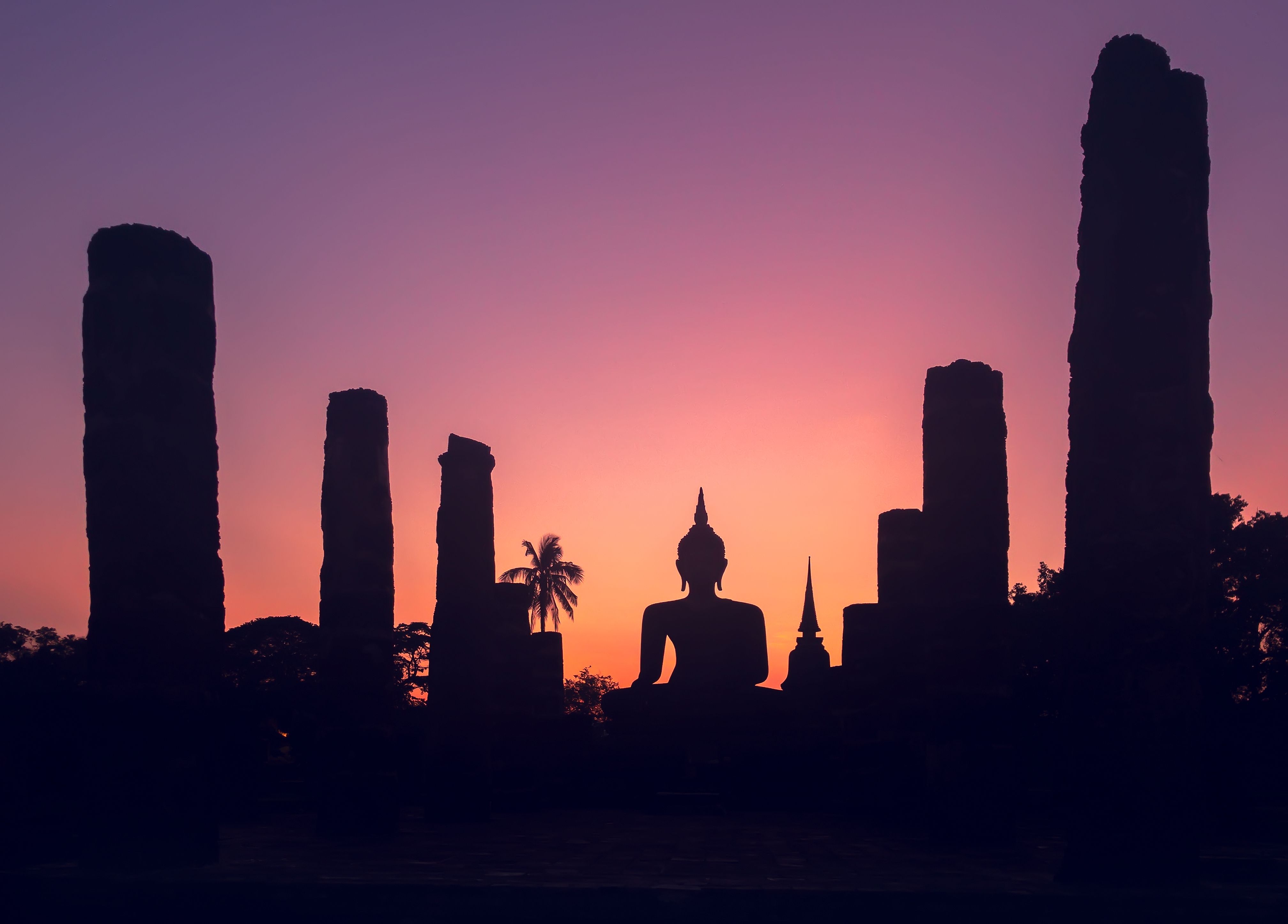Seated Buddha silhouetted among Sukhothai ruins at sunset