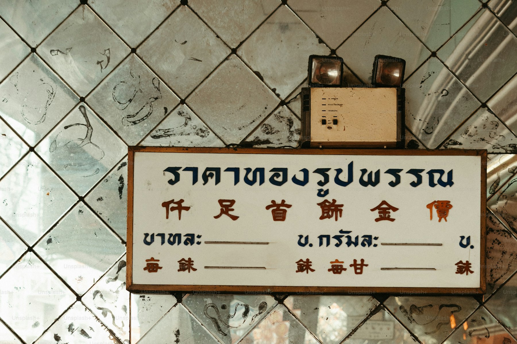 A hand-painted Thai gold-shop price board with Thai and Chinese script on mirrored tiles