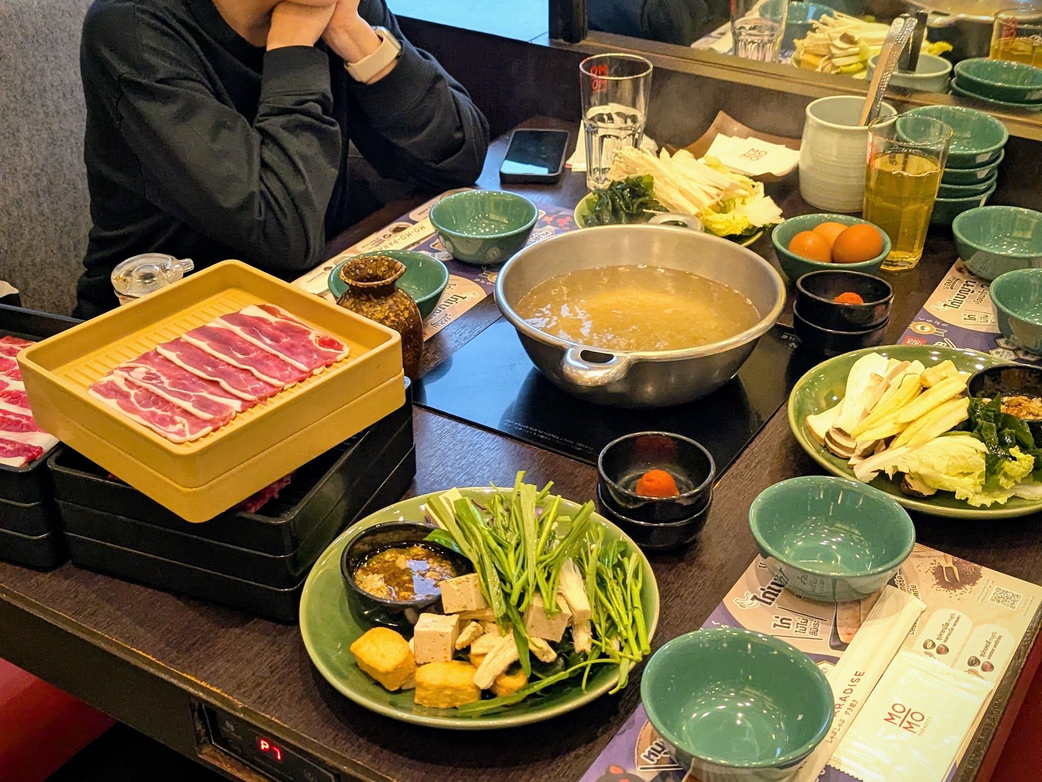 A bubbling shabu-shabu hot pot with plates of thinly sliced meat and vegetables at Mo-Mo-Paradise