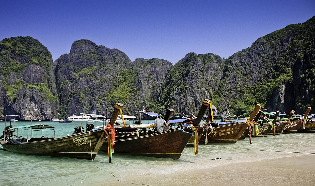 Longtail boats lined up on Maya Bay’s sand below the cliffs